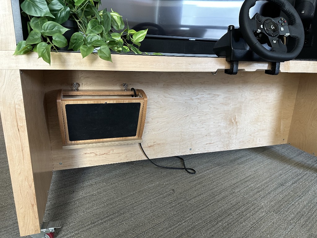 Custom plywood driving simulator desk on casters with Logitech wheel, monitor, and under-desk electronics enclosure